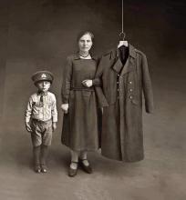 Une jeune femme et son enfant - la jeune femme tient le bras d'un manteau d'officier accroché à un cintre