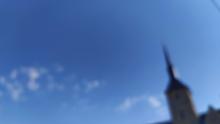 Un cliché flou dans lequel on distingue un clocher se détachant sur un ciel bleu